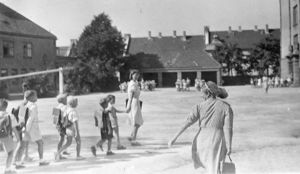 Første skoledag i 1947. Elevene taues til klasserommet av frøken. Det er seks gutter som går bak en ung dame i kjole i skolegården.