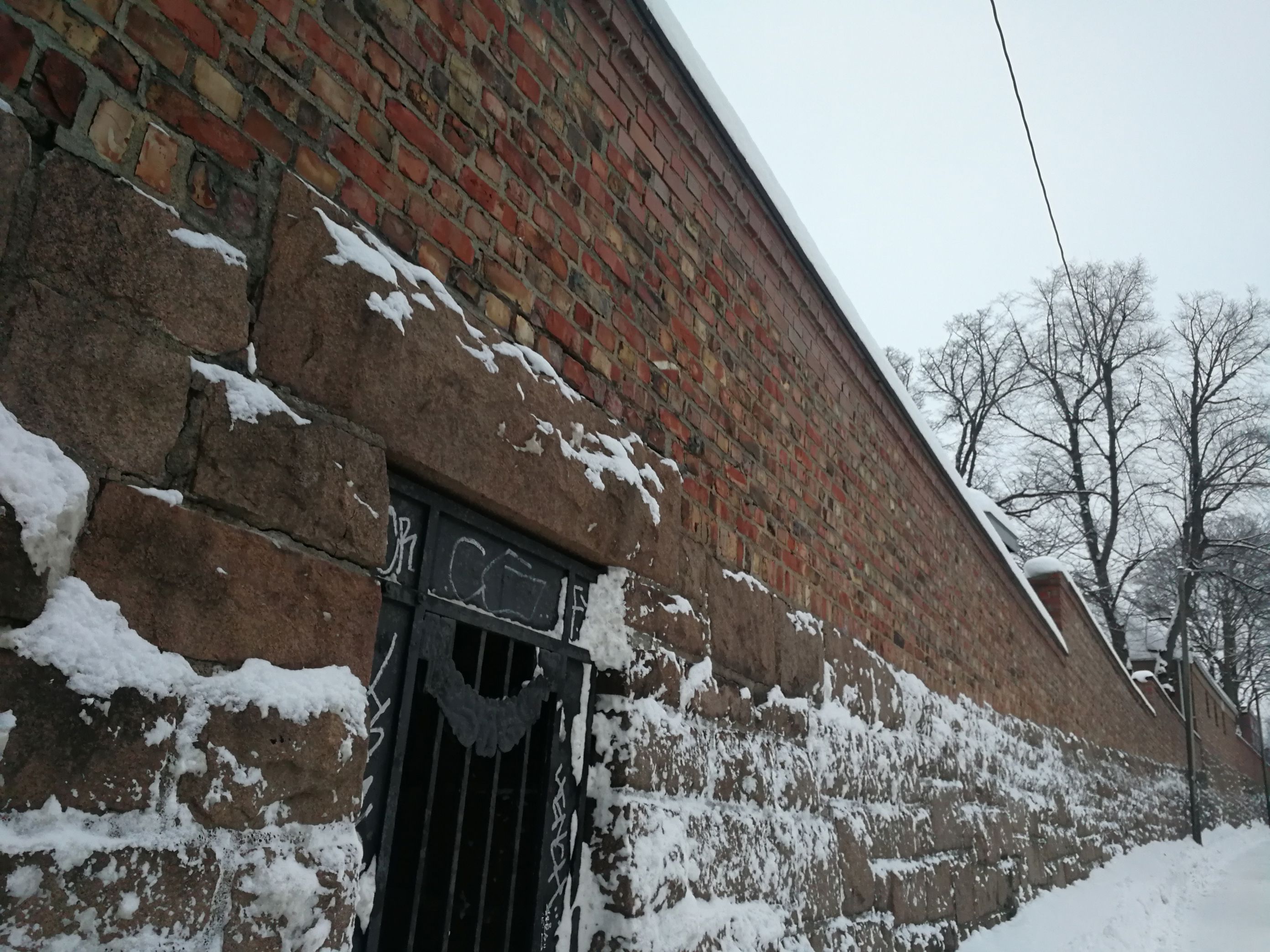 Bilde av muren langs skolegården i Dynekilgata. Muren er i rød murstein og det er snø langs kanten.