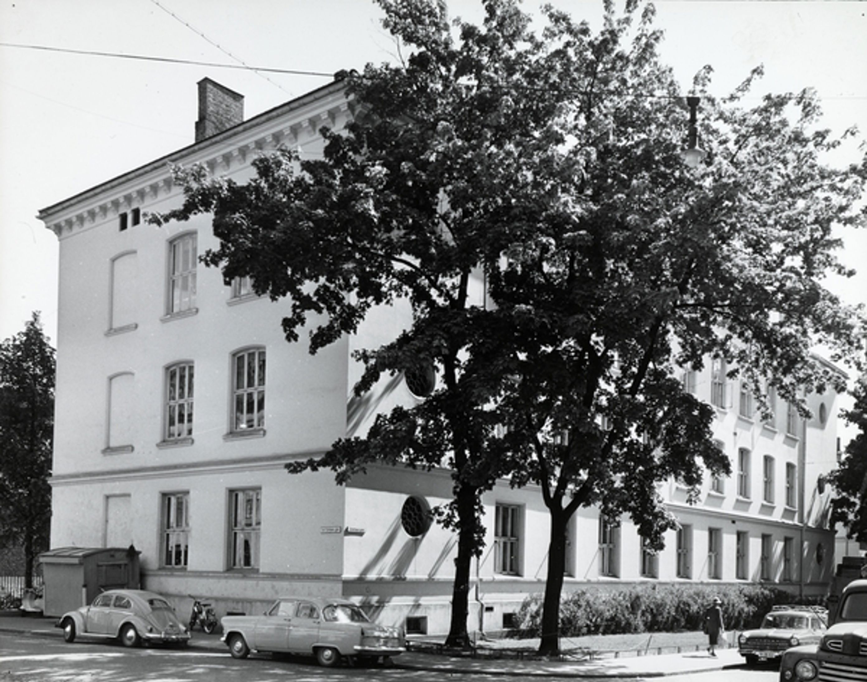 Bilde av Framhaldsskolen i 1961. To gammeldagse biler er parkert foran skolen.