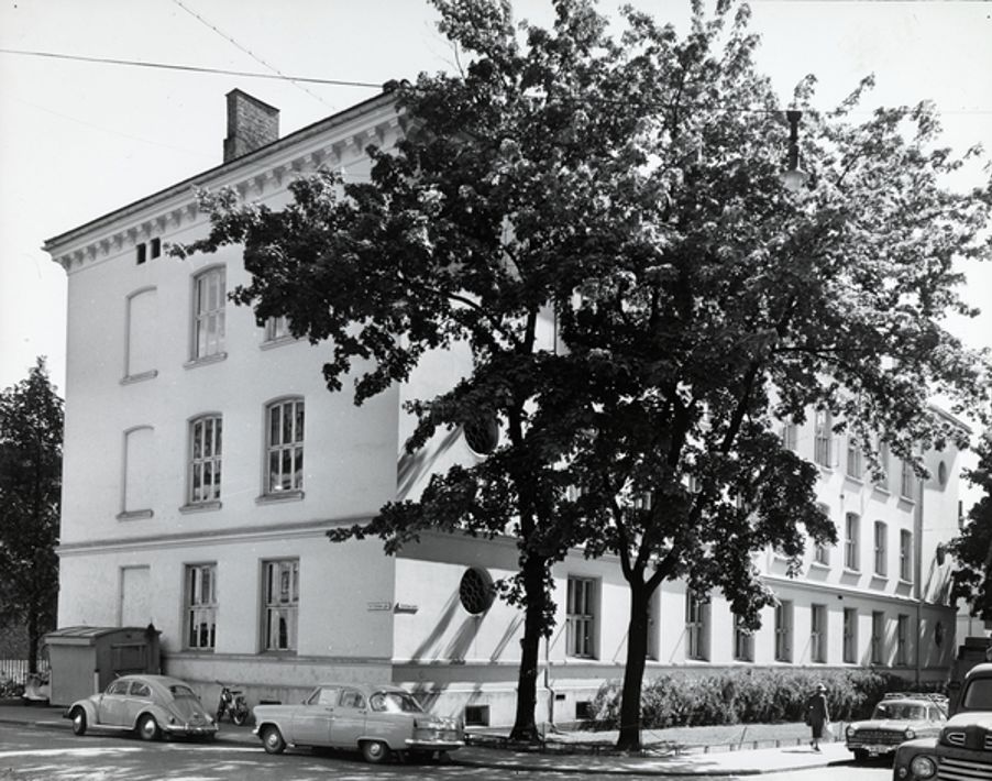 Foto: Framhaldsskolen, cirka 1961. Fotograf: Eidem, Olav Lorck. Oslo Museum/OB.FS0630 Bilde av Framhaldsskolen i 1961. To gammeldagse biler er parkert foran skolen.