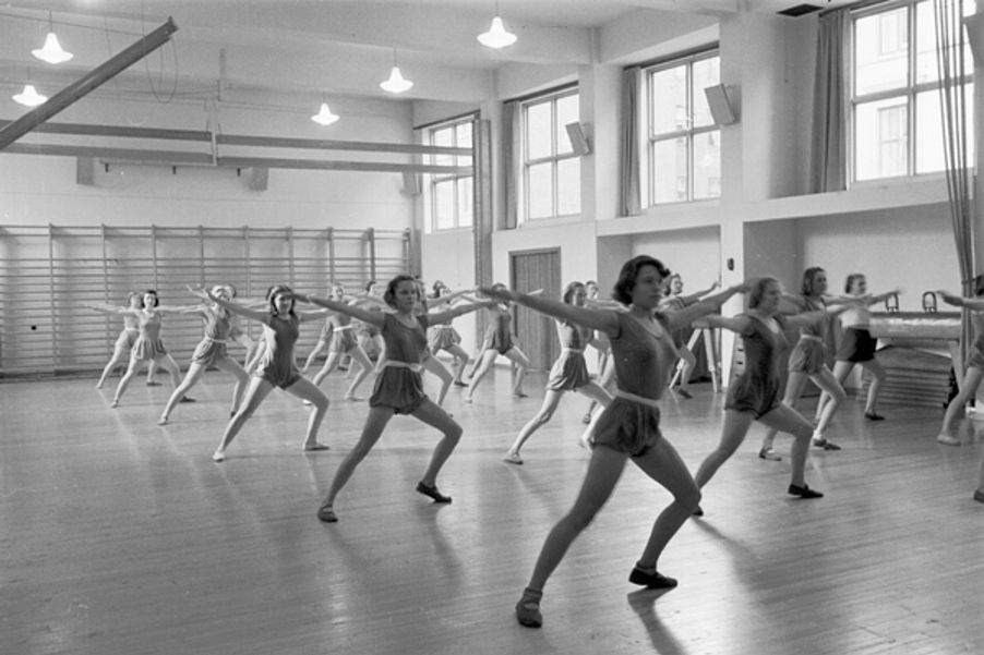 Foto: Fortsettelsesskole for piker, gymnastikk. Fotograf: Ukjent. Oslo byarkiv/A-20032/Ua/0004/010 Linjegymnastiakk på Osterhaus gate 22 i 1939. Pikene står med brede ben og begge armene ut til siden.
