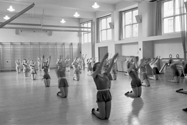 Fortsettelsesskole for piker, gymnastikk. 1939. Fotograf: Ukjent. Oslo byarkiv/A-20032/Ua/0004/009 Gymnastikk for piker i Osterhaus gate 22. Pikene sitter på knærne og strekker amene opp i taket.