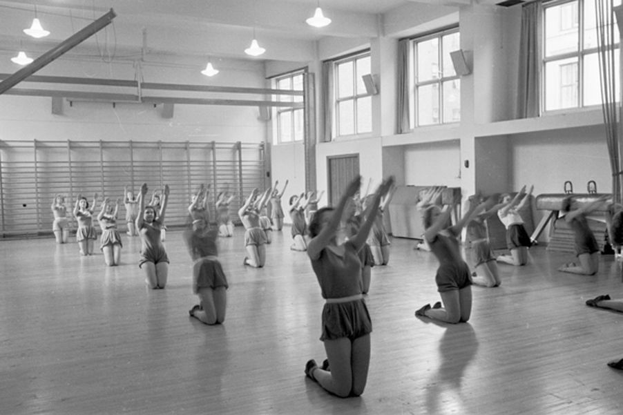 Foto: Fortsettelsesskole for piker, gymnastikk. 1939. Fotograf: Ukjent. Oslo byarkiv/A-20032/Ua/0004/009 Gymnastikk for piker i Osterhaus gate 22. Pikene sitter på knærne og strekker amene opp i taket.